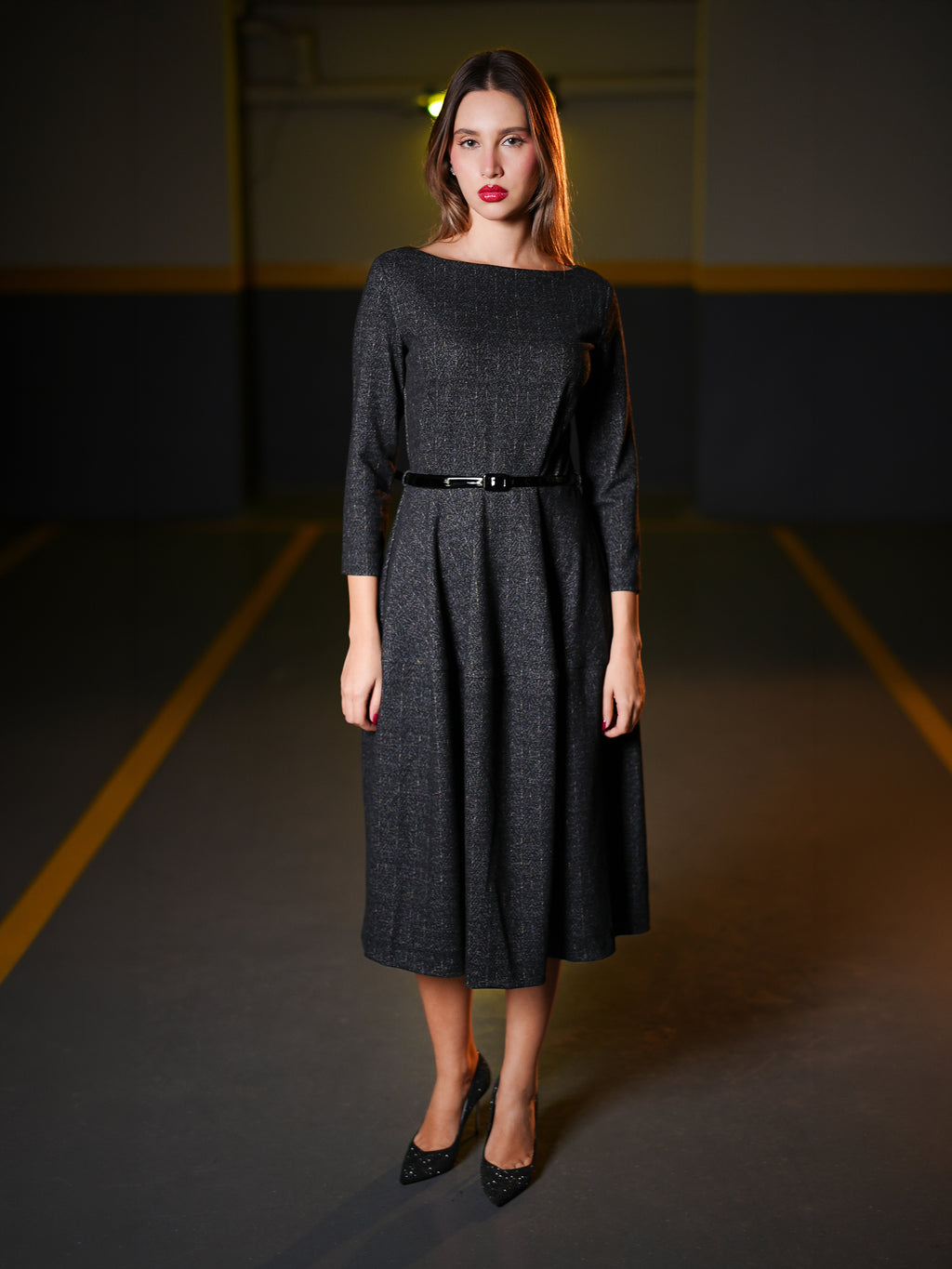 Wearing a dark charcoal gray textured midi dress with three-quarter sleeves, a boat neckline, and a thin black belt at the waist. 