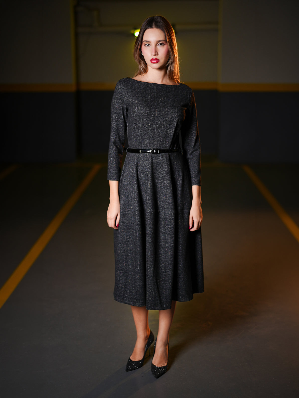 Wearing a dark charcoal gray textured midi dress with three-quarter sleeves, a boat neckline, and a thin black belt at the waist. 