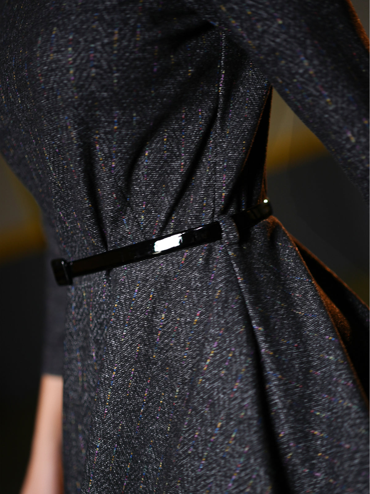 Close-up of a dark charcoal tweed dress with a thin black belt featuring a silver rectangular buckle.