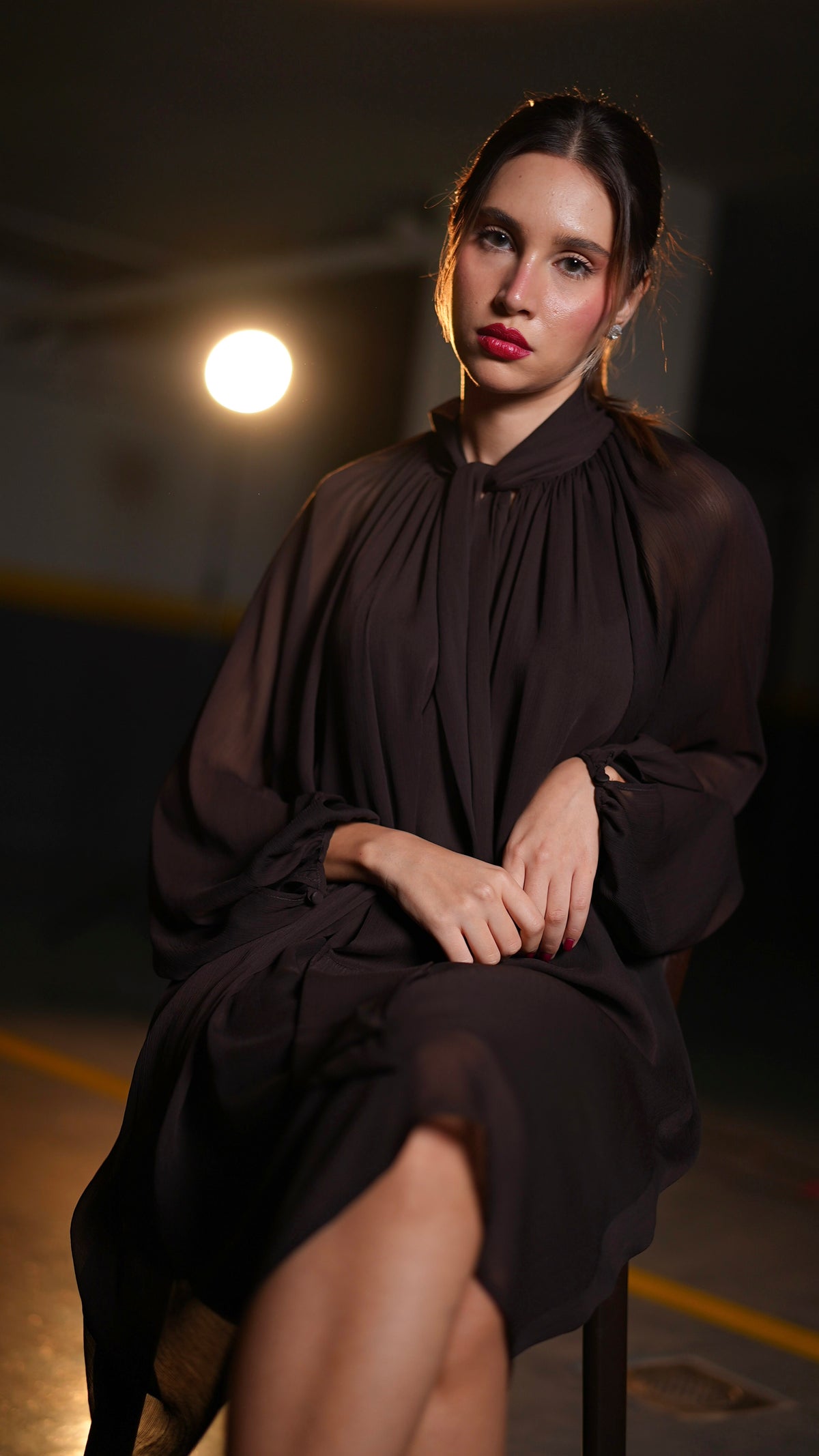 Dark chocolate-brown dress with gathered neckline and transparent sleeves, front view with model seated