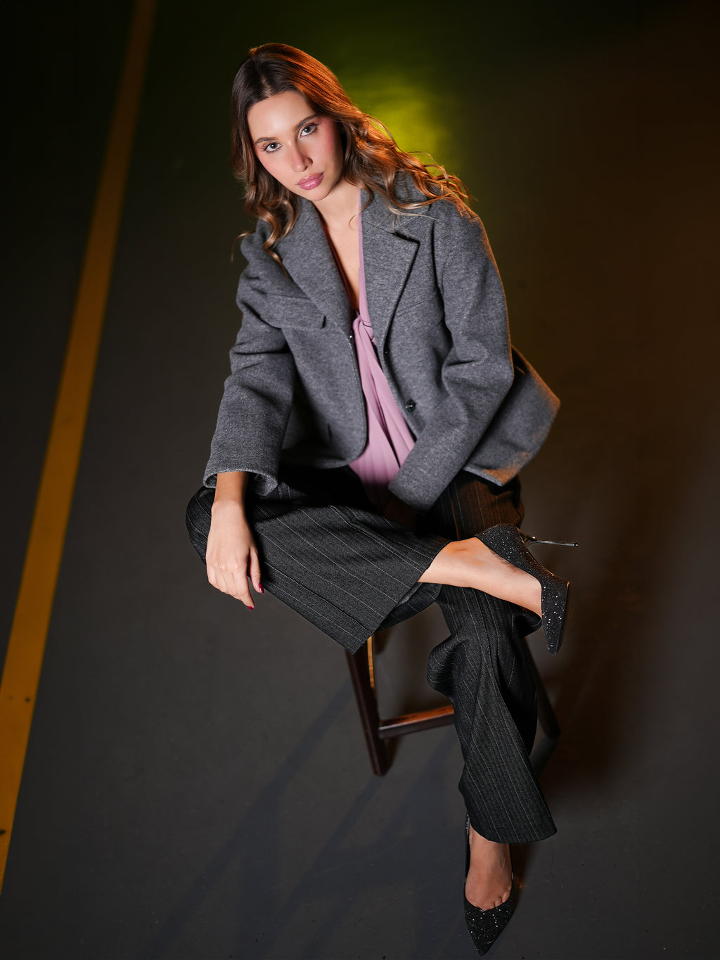 Grey wool cropped jacket with pinstripe trousers, seated full-length view